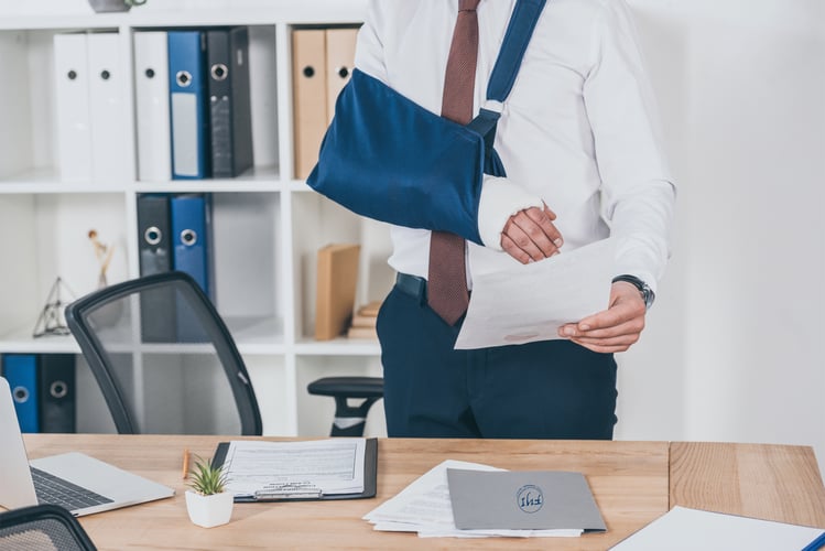 Injured office worker reviewing documents with arm in a sling, illustrating the importance of California workers’ compensation insurance for business owners in protecting employees and staying compliant.